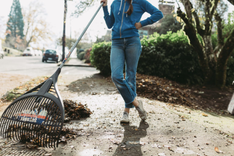 Woman raking leaves outside of her home.