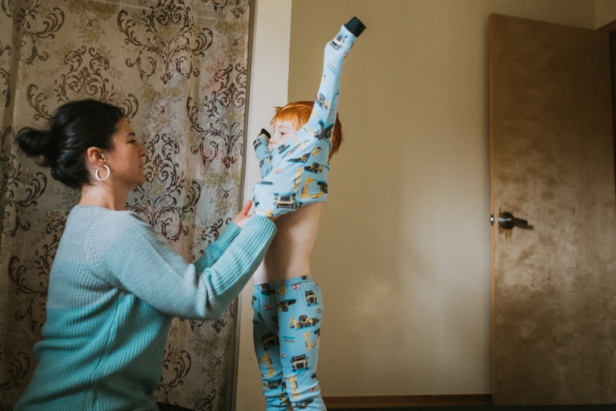 Woman helps put pajama shirt on little boy.