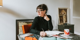 Woman wearing glasses sits at a desk and thinks about something.