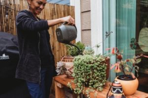 Woman watering potted plants outside her home.