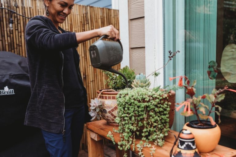 Woman watering potted plants outside her home.